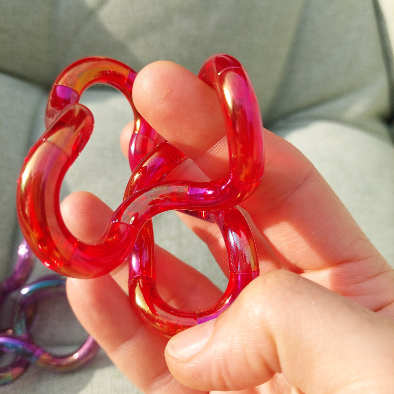 diep rode tangle gems in hand, fidget friemelen. Zon schijnt, achtergrond groen tuinstoelkussen en paarse tangle gems