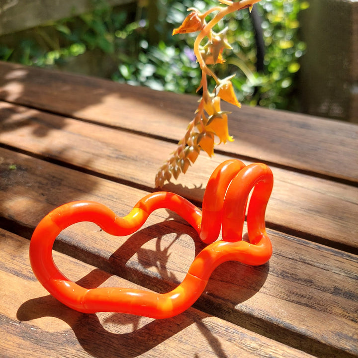 new tangle marble oranje rood, op houten tafel voor oranje bloem, fidget, friemelspeelgoed, motoriek sensoriek materiaal