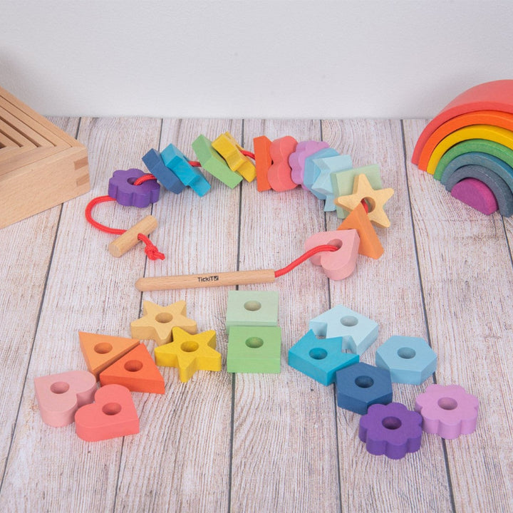 houten speelgoed van ticket met rijg vormen in regenbogenkleuren en veter met rijghulpnaald